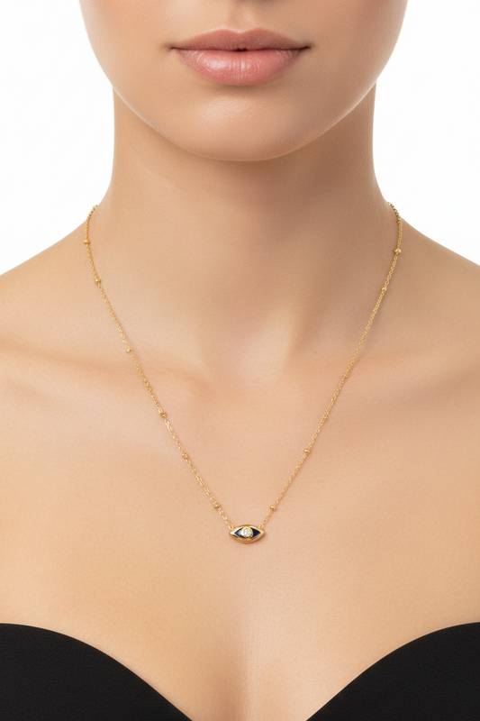 A gold chain necklace featuring a small evil eye pendant with a black center and a clear stone, shown against a plain white background.