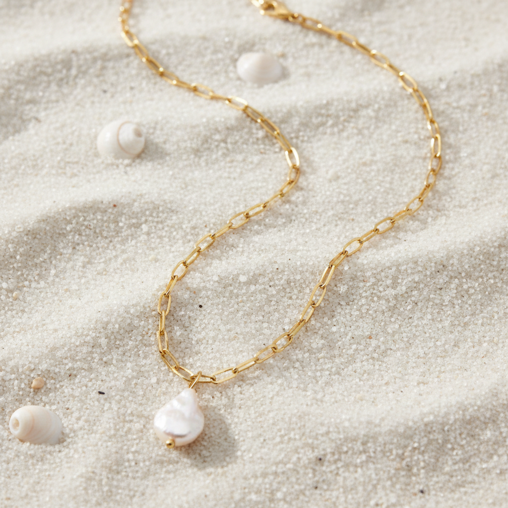 A gold paperclip chain necklace with a small, irregular white pearl pendant, displayed on a clean white background.