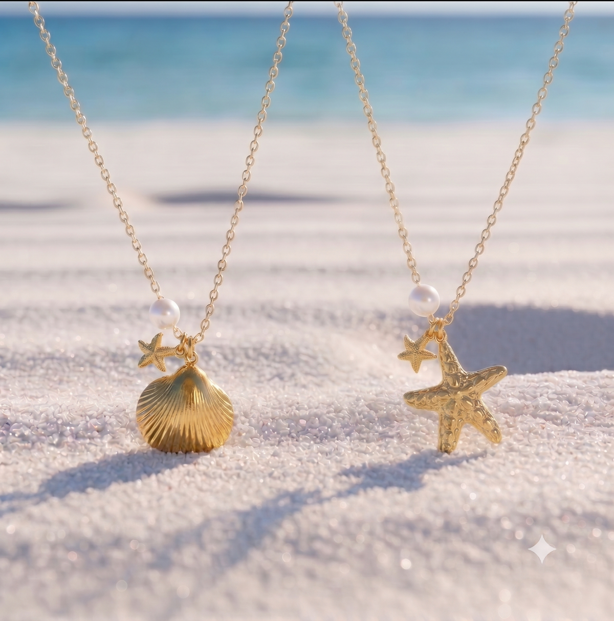 Two gold-toned necklaces resting on white sand at the beach, one with a sea scallop shape and starfish pendant and the other with a starfish pendant, both hanging near the waterline.